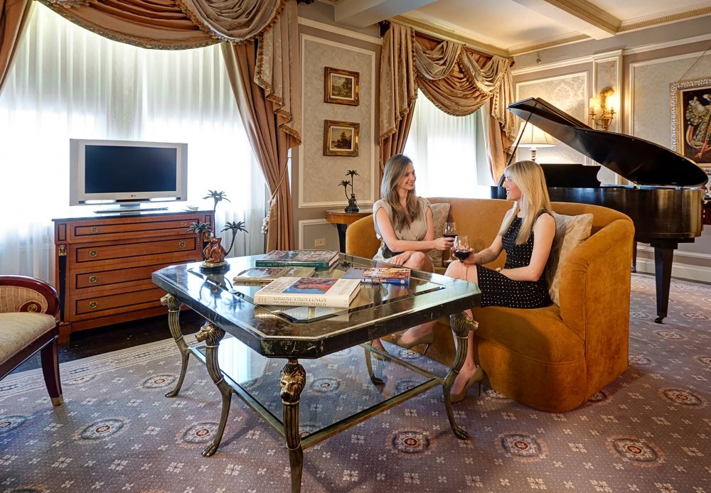 women sitting on couch drinking wine with piano behind them